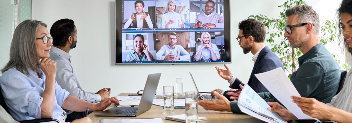 Diverse company employees having online business conference video call on tv screen monitor in board meeting room