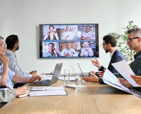 Diverse company employees having online business conference video call on tv screen monitor in board meeting room